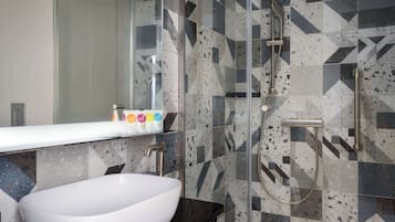 A bathroom with a white sink, a glass shower enclosure, and a tiled wall with geometric patterns.