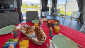 A breakfast table set with bread, eggs, juice, and fruit in a bright room with a view of a garden and a house. - 2 bedroom stunning home in Lauwersoog (Lauwersoog)