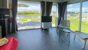 A modern room with a large window, a flat-screen TV, a small table, a bench, and a red towel on a table. - 2 bedroom stunning home in Lauwersoog (Lauwersoog)
