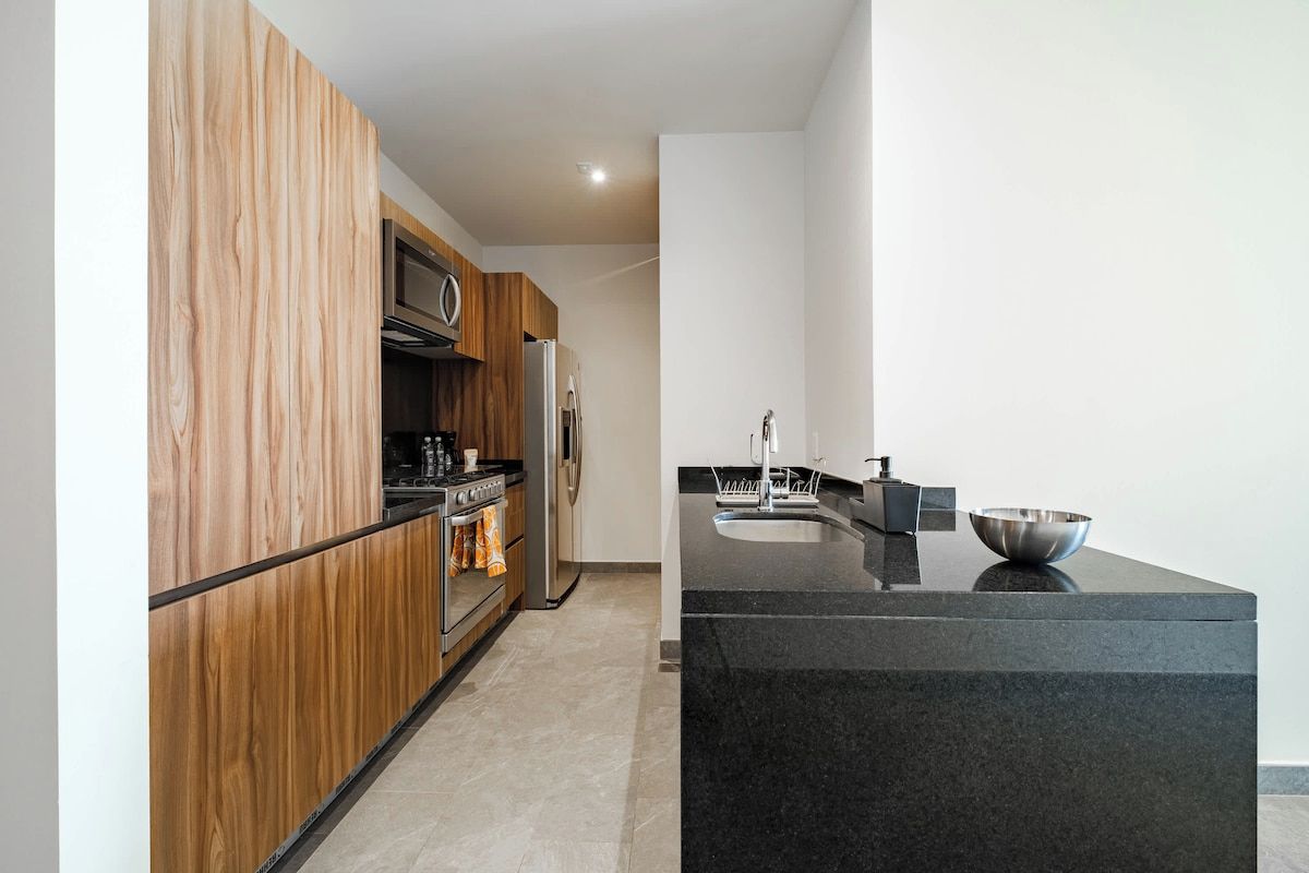 A modern kitchen with wooden cabinetry, stainless steel appliances, and a black granite countertop.