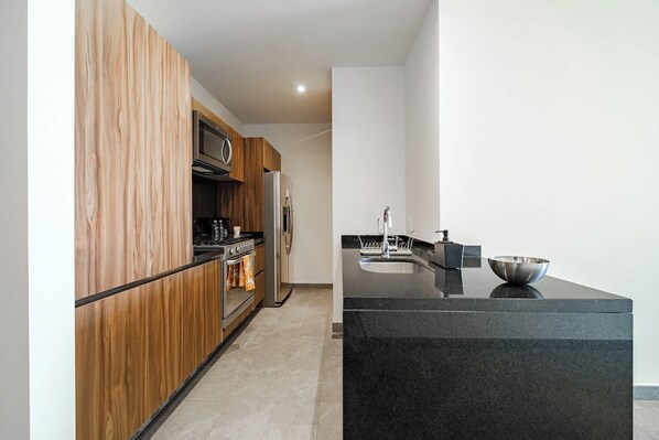 A modern kitchen with wooden cabinetry, stainless steel appliances, and a black granite countertop.