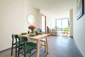 A dining area with a table set for four, chairs, a vase with flowers, and a large window in the background.