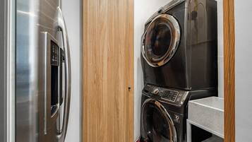 A compact laundry area with a stainless steel refrigerator and a stacked washer and dryer.