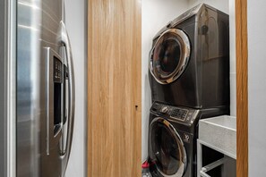 A compact laundry area with a stainless steel refrigerator and a stacked washer and dryer.