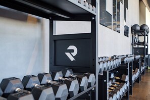 A gym with weightlifting equipment, including dumbbells and barbells, and a wall-mounted rack.