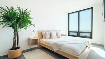 A modern bedroom with a bed, bedside tables, a potted plant, and a large window.