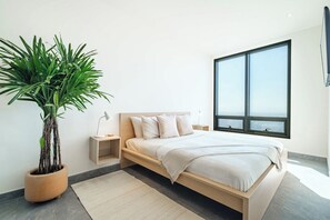 A modern bedroom with a bed, bedside tables, a potted plant, and a large window.