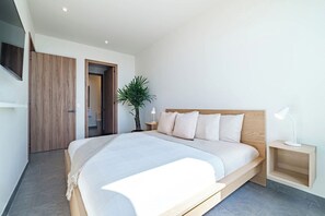 A modern bedroom with a large bed, a bedside table, a nightstand, a potted plant, and a wooden wardrobe.