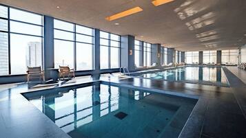 A large indoor swimming pool with clear glass walls, allowing views of the cityscape.