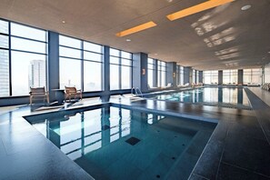 A large indoor swimming pool with clear glass walls, allowing views of the cityscape.