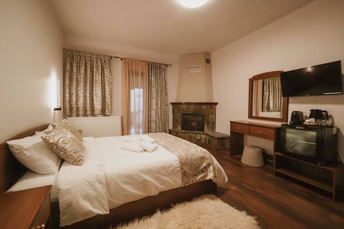 Een slaapkamer met een bed, een open haard, een televisie en een bureau.