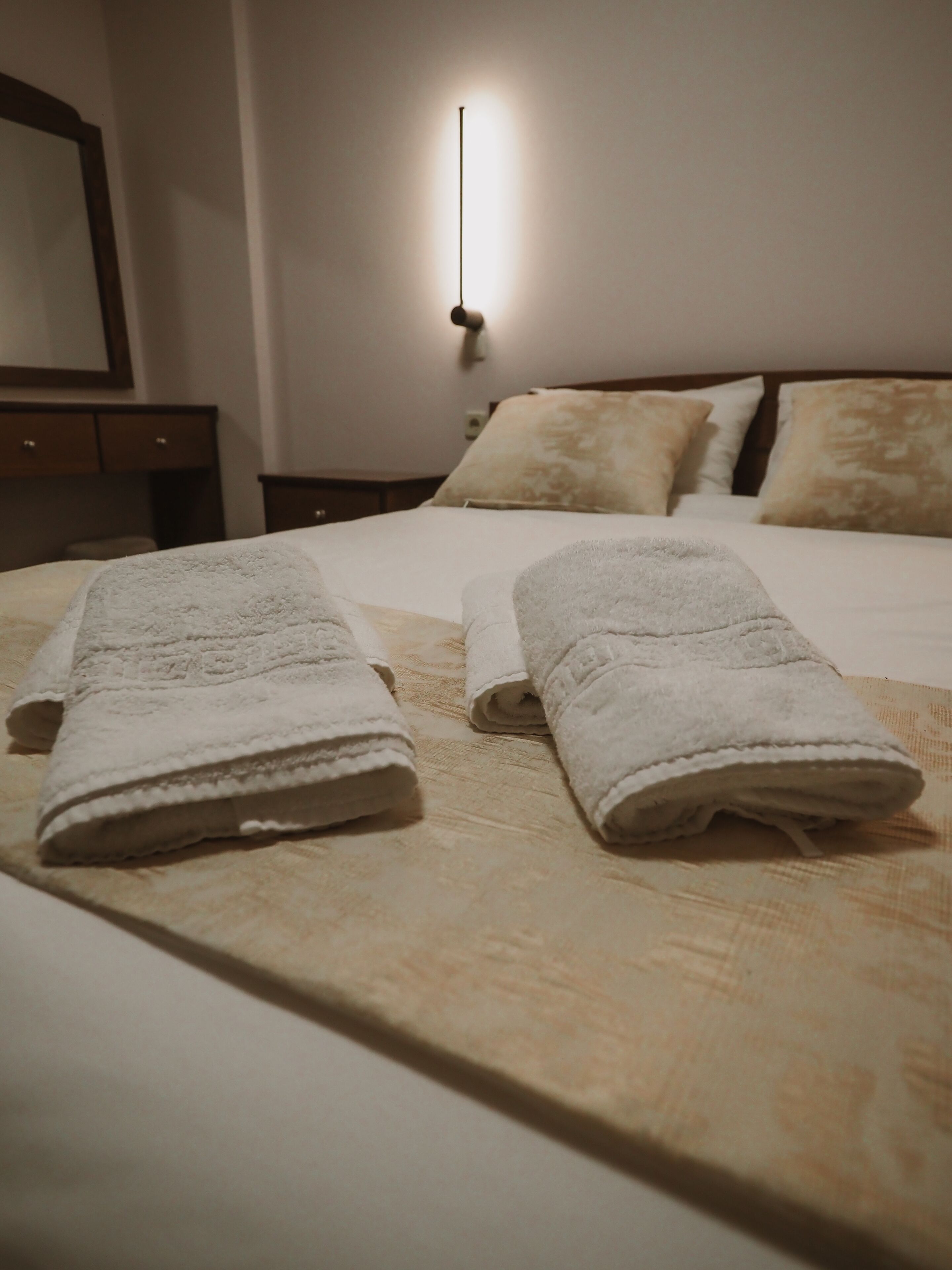 A neatly made bed with two rolled towels and a bedside table with a lamp.
