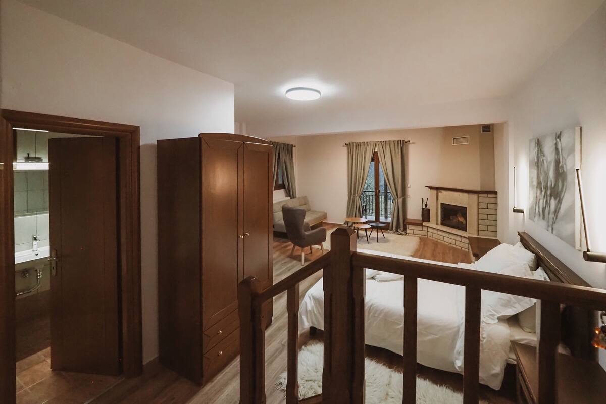 Een ruime slaapkamer met een grote kledingkast, een gezellige zithoek met een open haard, en een balkon met gordijnen.
