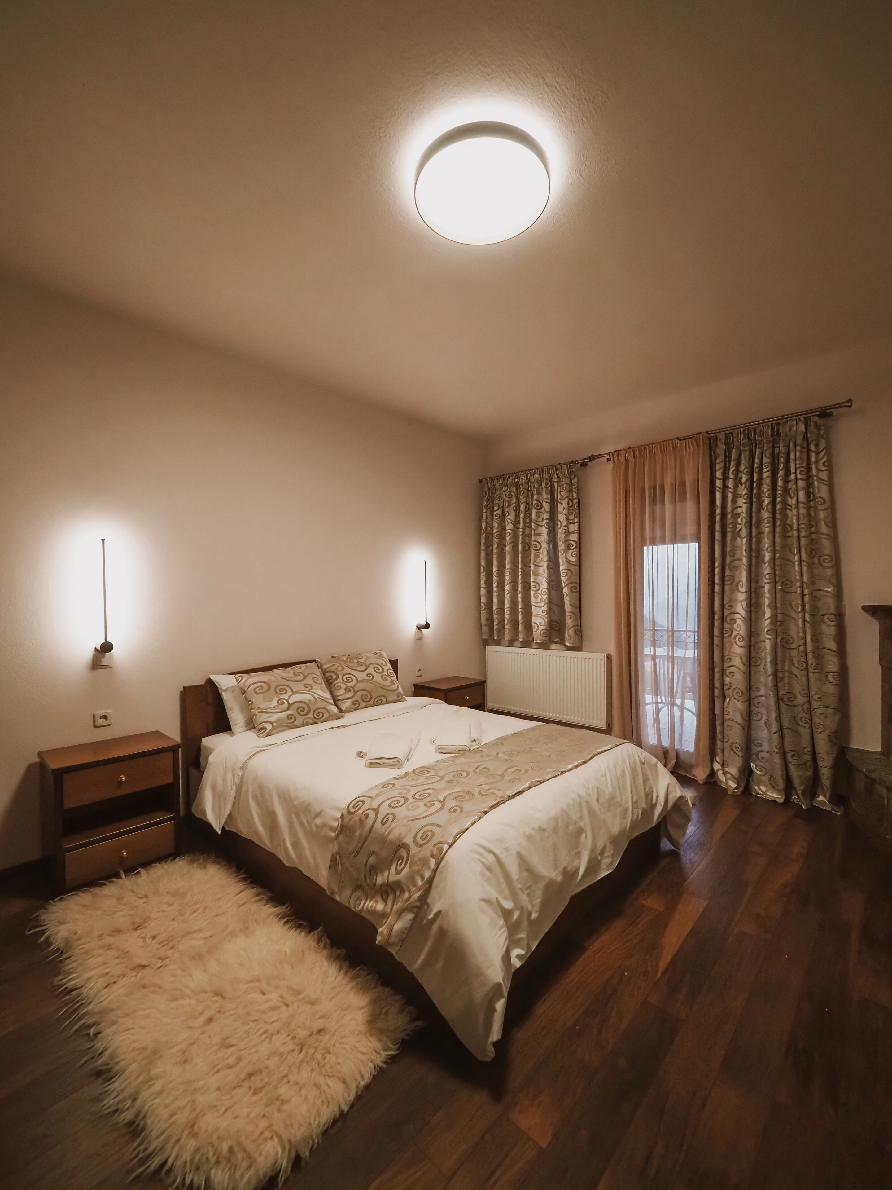Un dormitorio con cama, mesitas de noche, una alfombra mullida, un radiador y cortinas.