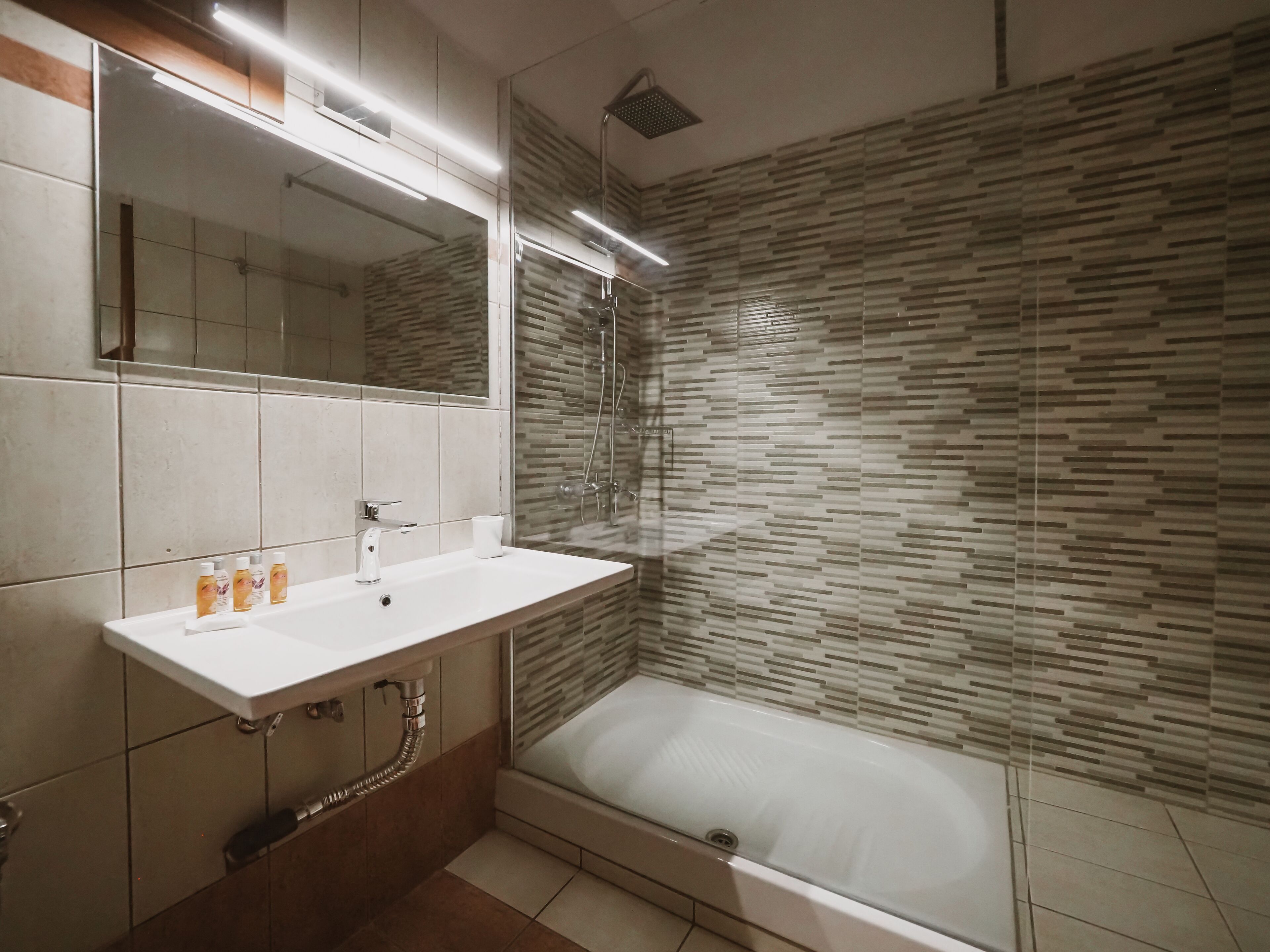 Een moderne badkamer met een wit wastafeltje, spiegel en douche.