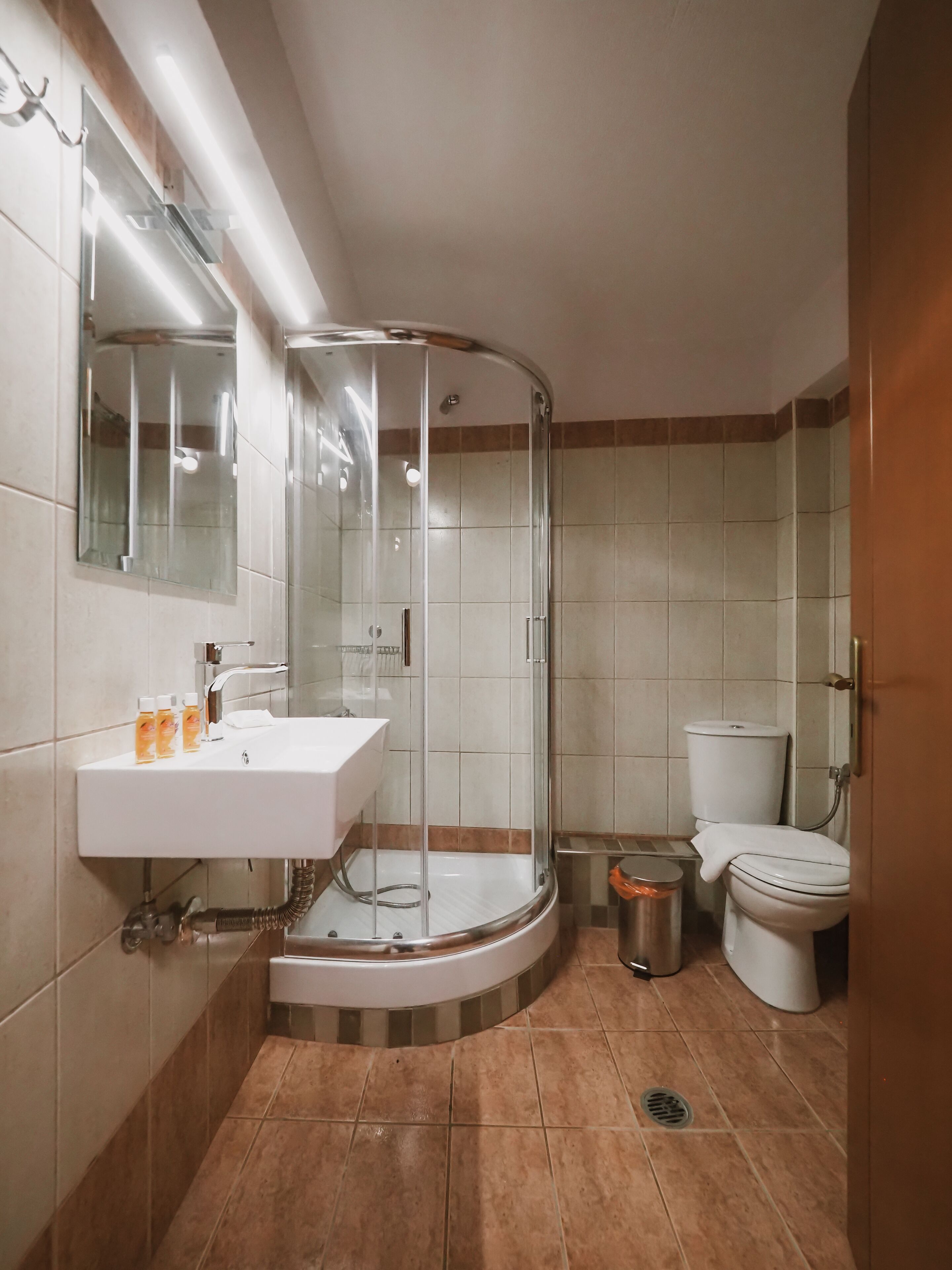Un baño moderno con ducha de vidrio, un lavabo blanco con artículos de aseo y un inodoro.