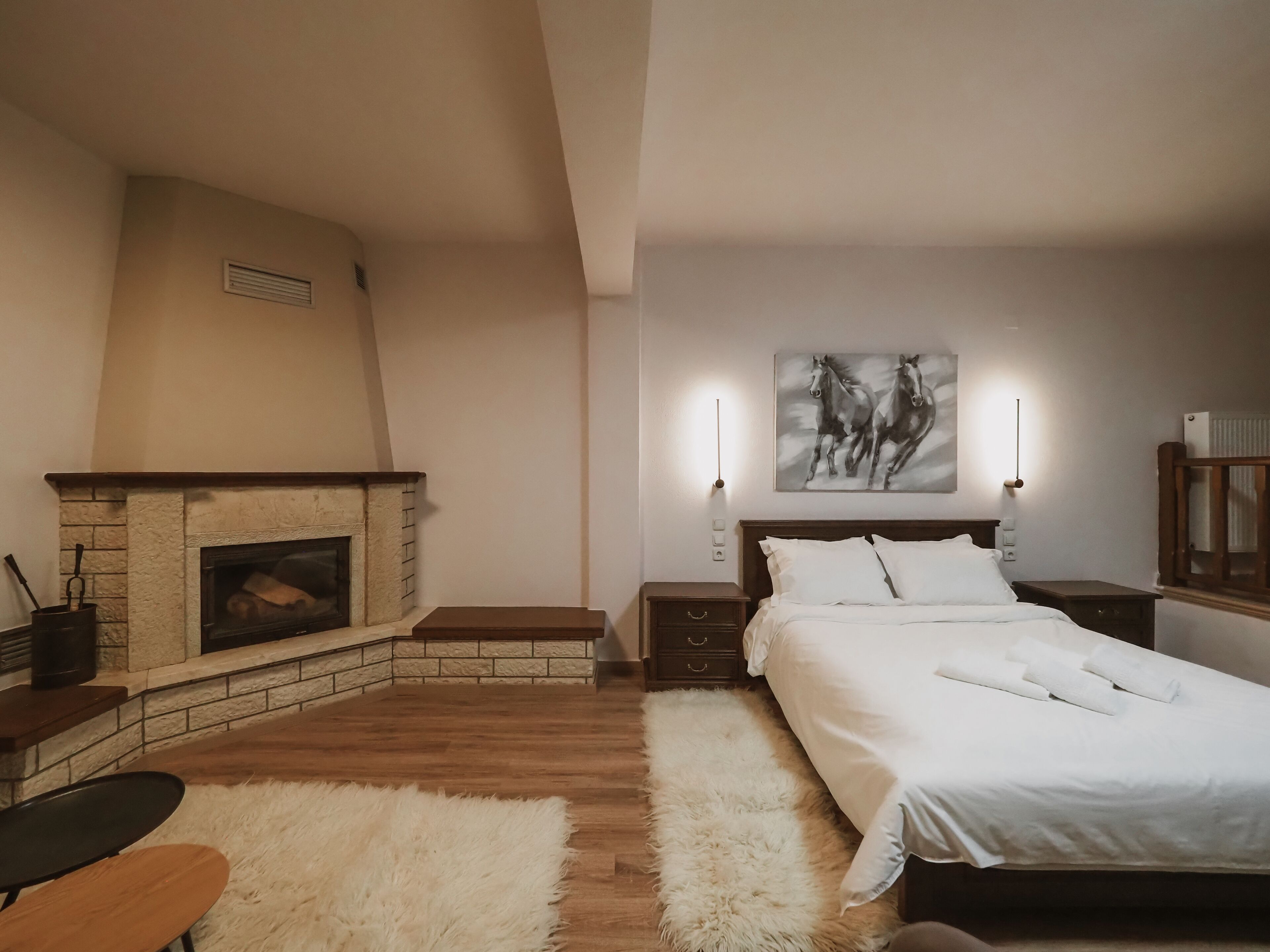 Ein Schlafzimmer mit Kamin, einem Bett mit weißer Bettwäsche, einem flauschigen Teppich und einem Gemälde von Pferden an der Wand.