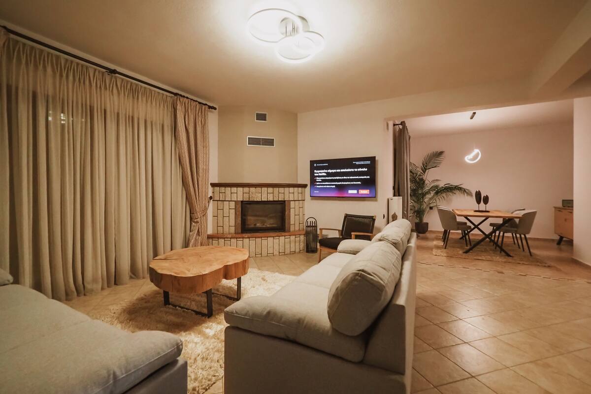 Een woonkamer met een bank, salontafel, open haard, televisie en een eethoek met stoelen en een tafel.