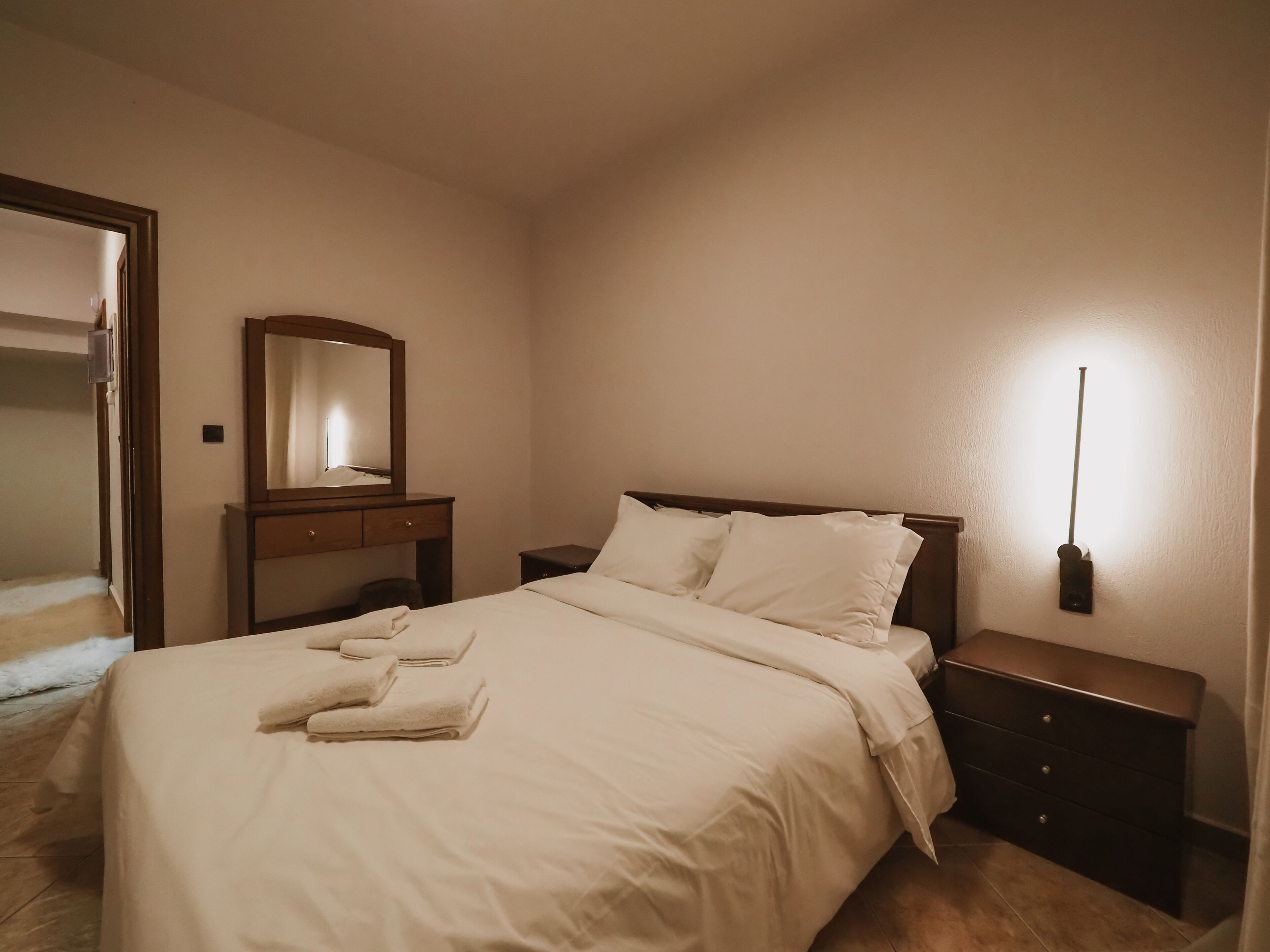 Habitació d'hotel amb llit, taulell de nit, prestatge i mirall, més una làmpada penjada a la paret.