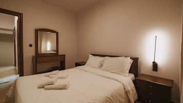 Habitació d'hotel amb llit, taulell de nit, prestatge i mirall, més una làmpada penjada a la paret.