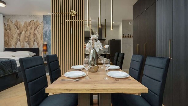 Un espace repas moderne avec une table en bois, des chaises à revêtement noir et un vase rempli de fleurs blanches.