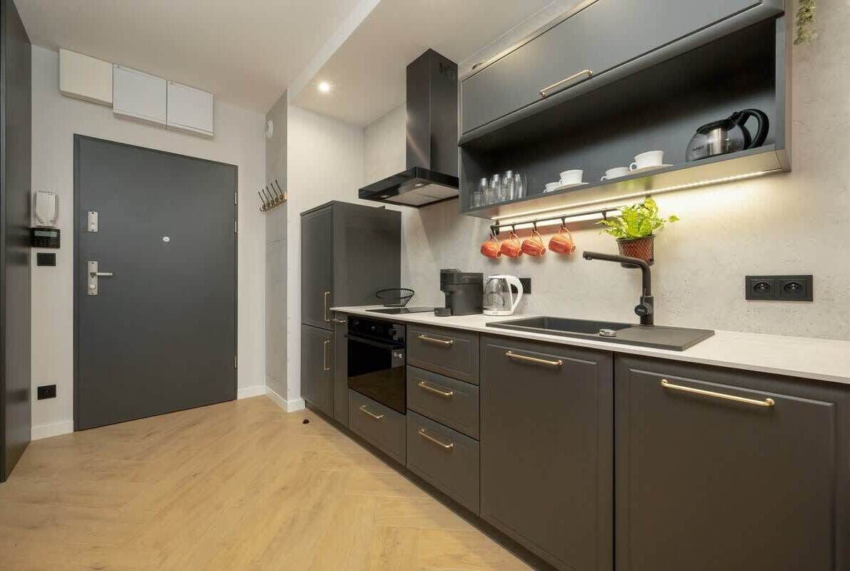 Une cuisine moderne avec des meubles de rangement sombres, un four encastré, un évier et un plan de travail.