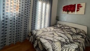 Ein Schlafzimmer mit Bett, Vorhängen, einer Klimaanlage und einem an der Wand befestigten Kunstwerk.