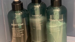 Drei Flaschen Badesseife, Shampoo und Conditioner auf einer transparenten Oberfläche.