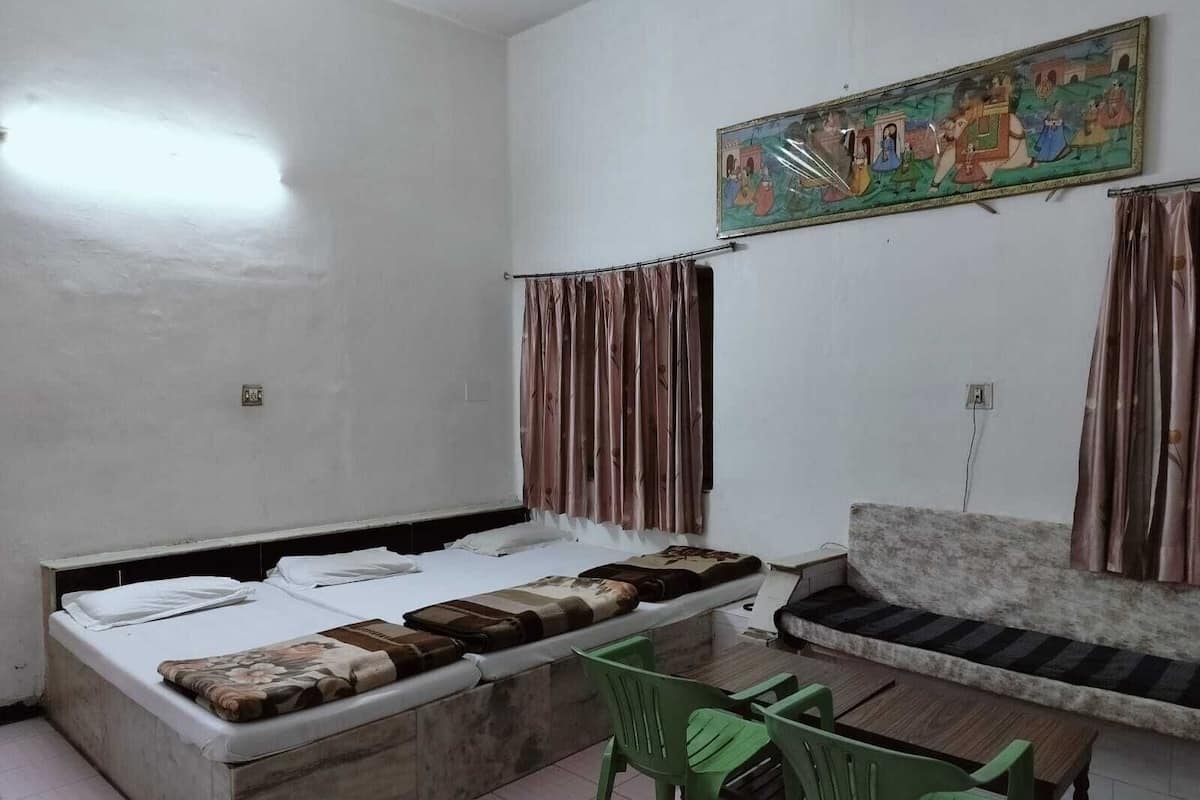 A room with a bed, a sofa, and two green chairs. There is a painting on the wall and curtains on the windows.