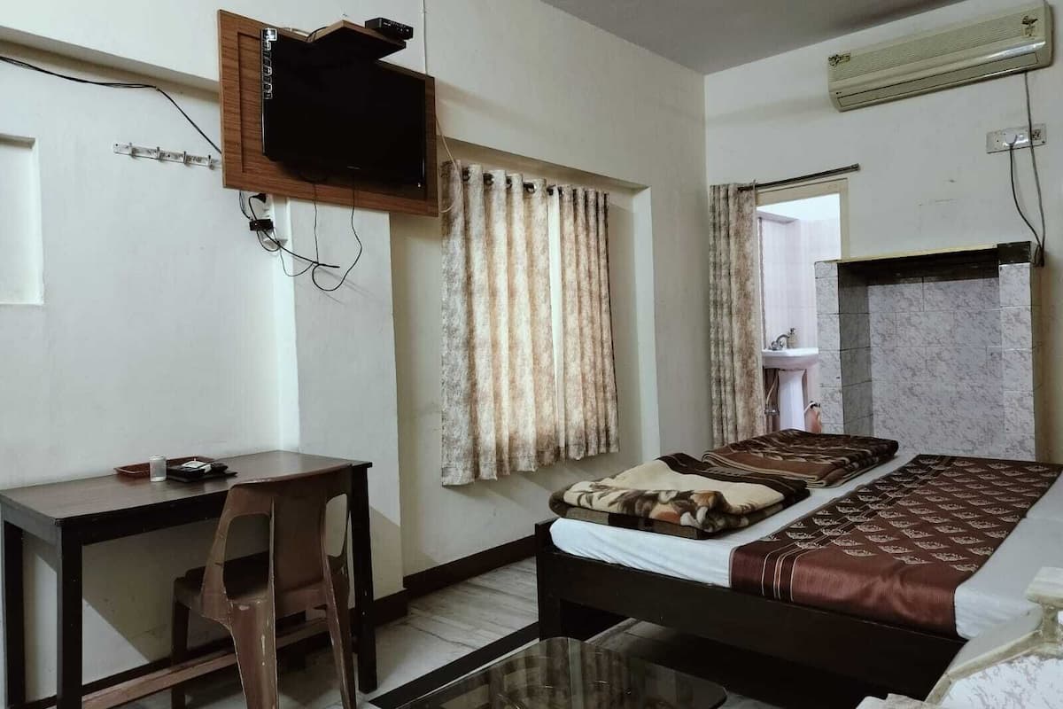 A bedroom with a bed, a desk, a chair, a TV mounted on the wall, and an air conditioner.