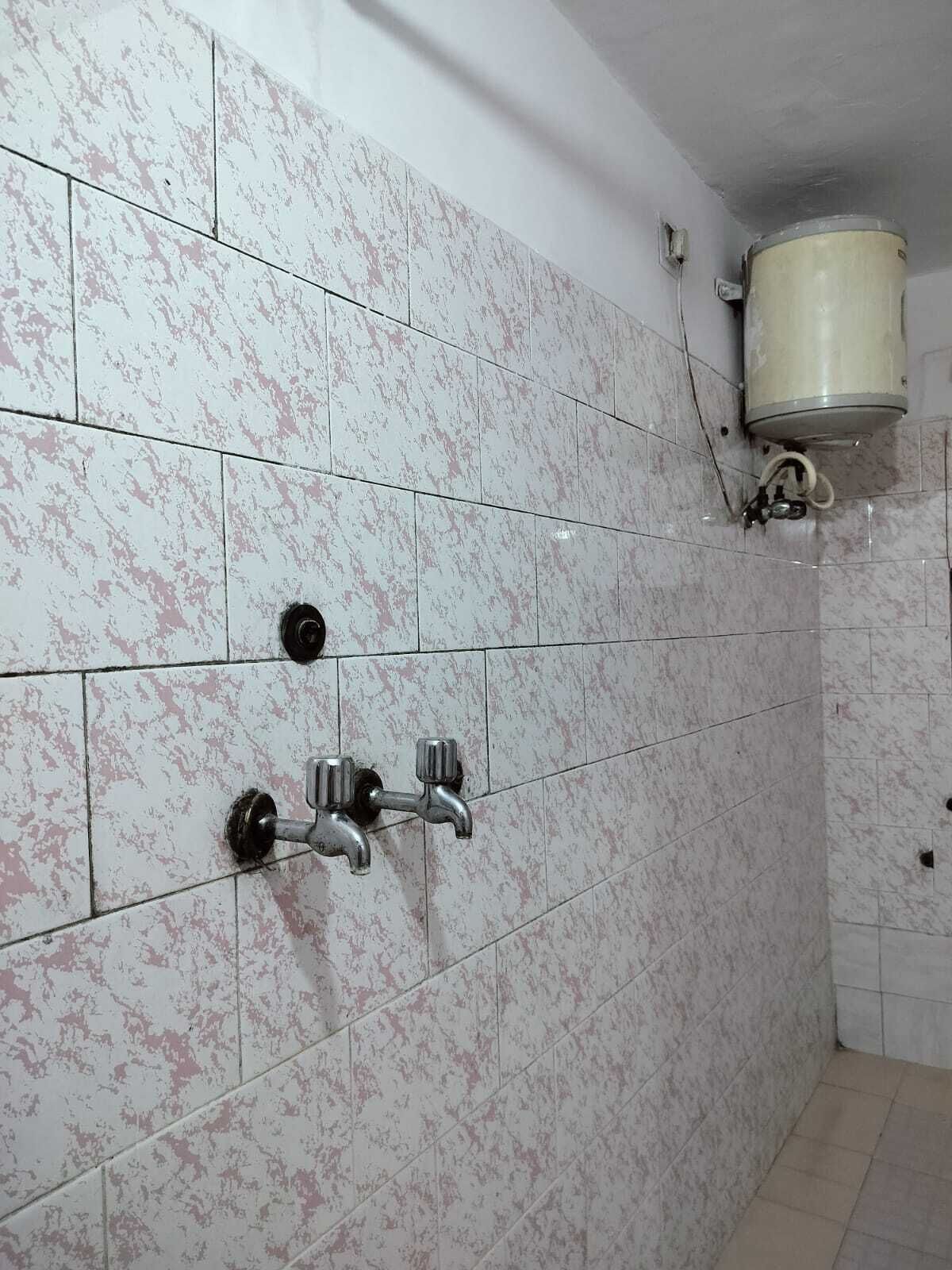A bathroom with white marble tiles, a shower with a faucet, and a water heater mounted on the wall.