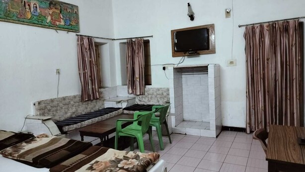 A room with a sofa, a television mounted on the wall, a fireplace, and curtains. - Hotel Rawat (Jodhpur)
