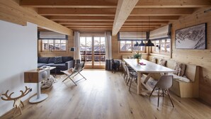 Una habitación amplia con vigas de madera, una mesa de comedor con sillas, un sofá y un ventanal con vistas a las montañas.