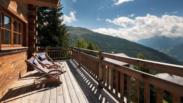 Una terraza de madera con sillas de descanso y barandilla de madera, con vistas a un paisaje montañoso.