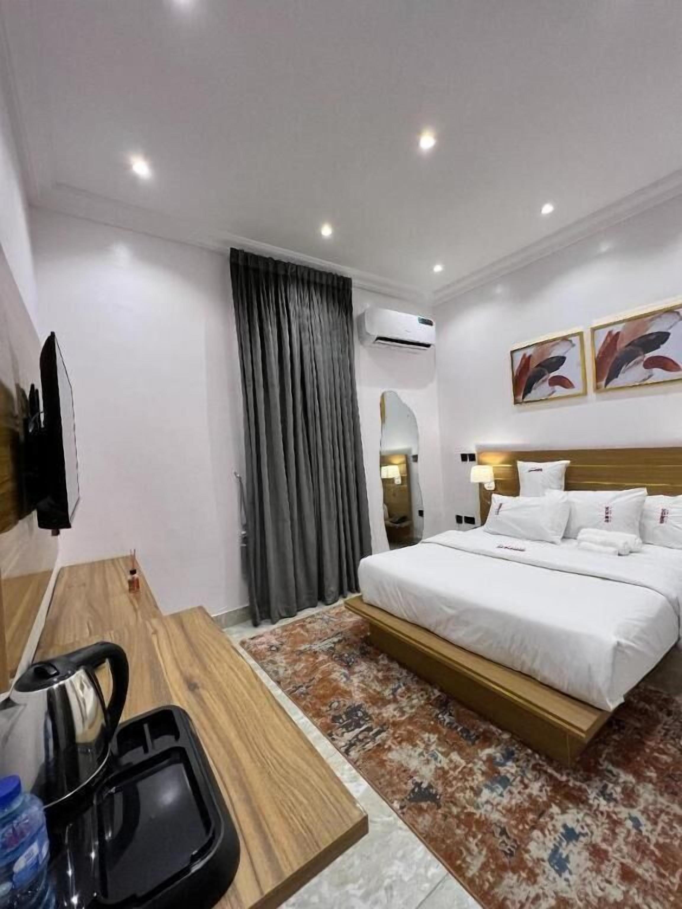 Een hotelkamer met een bed, een bureau met waterkoker, een waterfles en een kamerkleed met dessin.