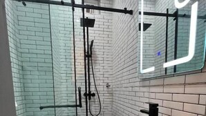 Une salle de bain moderne avec une douche à l’italienne en verre, des toilettes blanches et un meuble-lavabo avec un miroir.