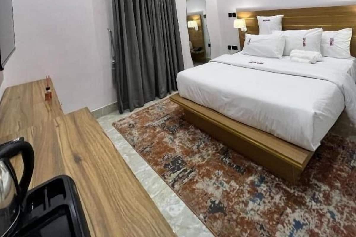 Quarto de hotel com cama, escrivaninha, cadeira, ar condicionado e duas pinturas na parede.