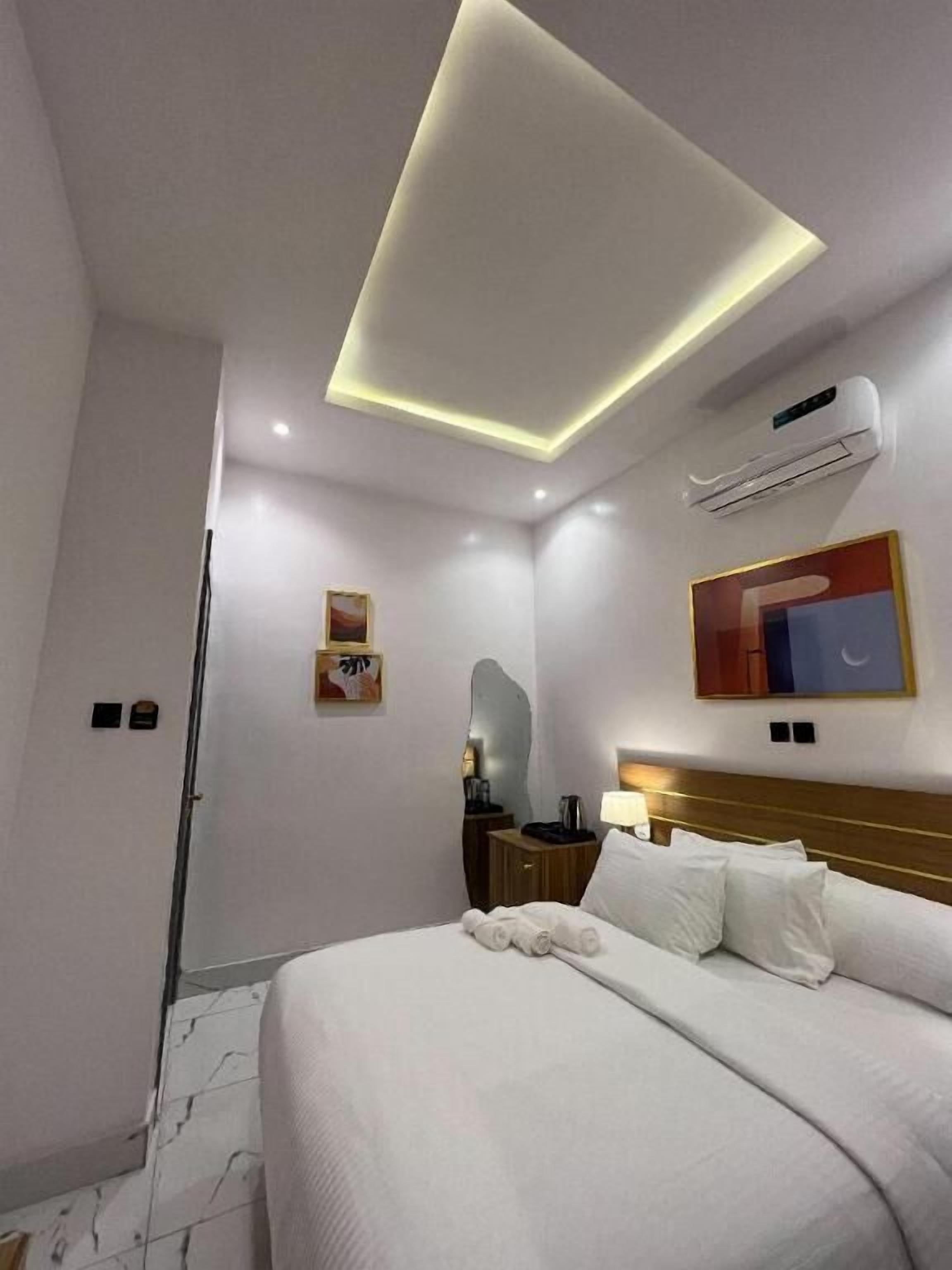 Een moderne hotelkamer met een groot bed, een nachtkastje met een lamp, een wandairconditioner en een plafondlamp.