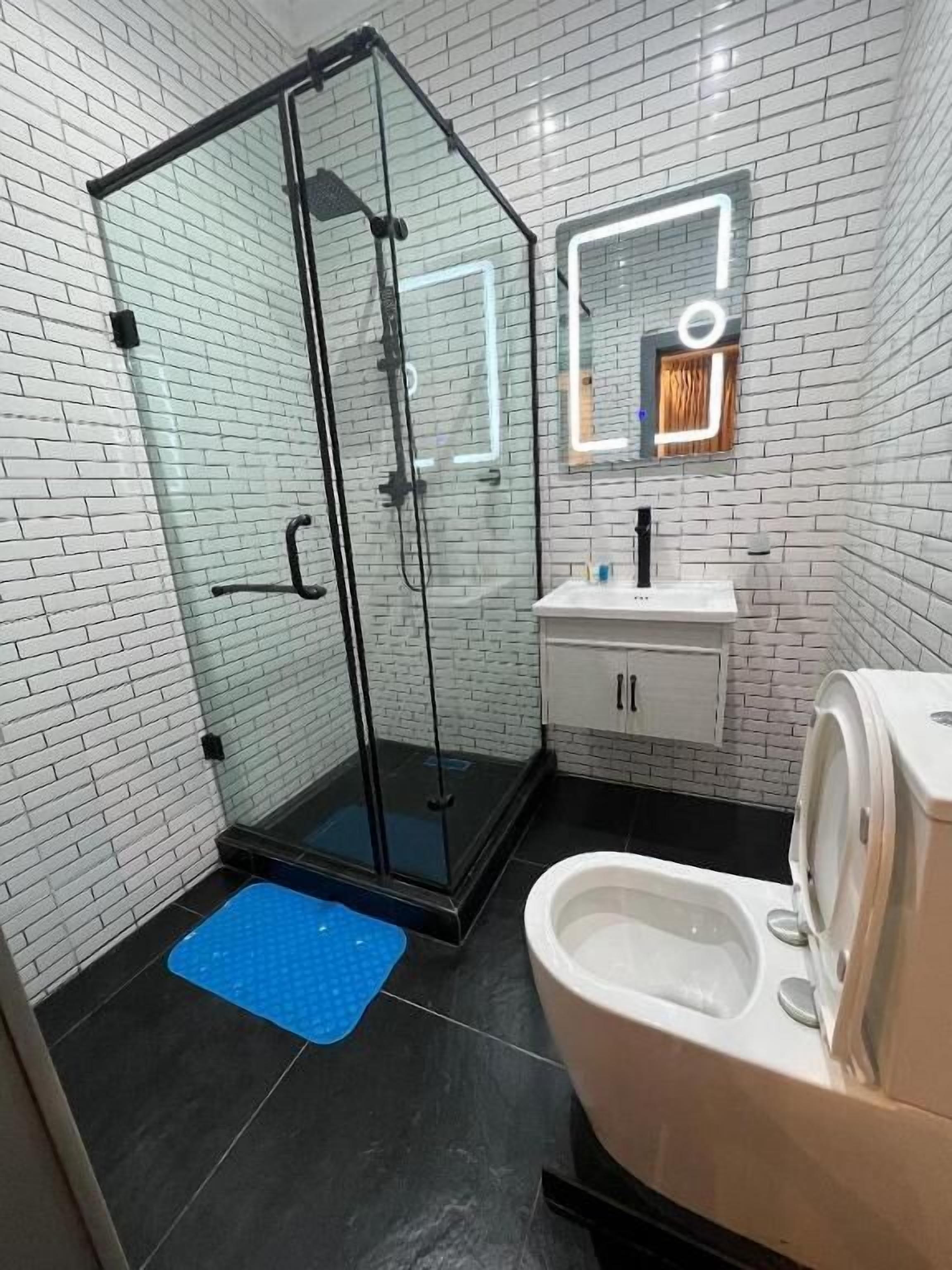 A modern bathroom with a glass-enclosed shower, white tiled walls, a white sink, and a toilet.