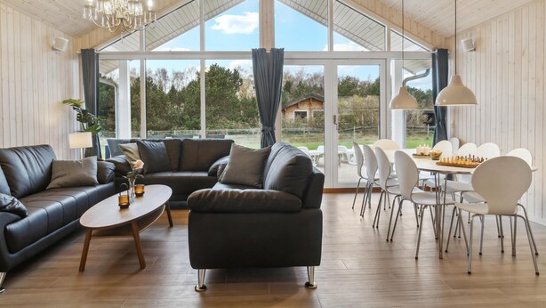Un salon spacieux avec une grande fenêtre, un canapé en cuir noir, une table à manger avec des chaises et un lustre.