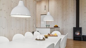 Un espace repas moderne avec un mur en bois, deux lampes suspendues, une table blanche et une cheminée.