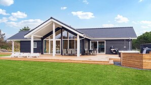 Une maison moderne dotée d’un patio couvert, de grandes fenêtres et d’une pelouse bien entretenue.
