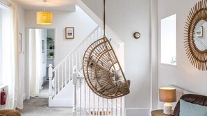 Um interior moderno com uma cadeira de rattan suspensa, uma escada e um objeto decorativo na parede.
