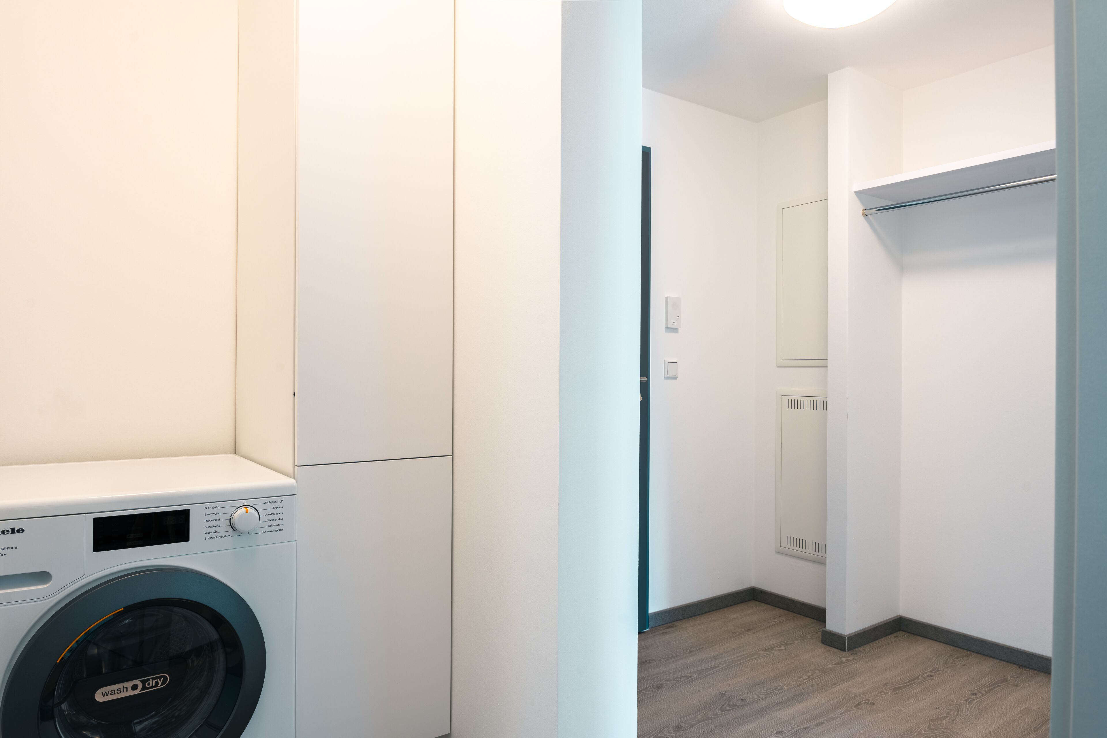 A laundry area with a front-loading washing machine, a mirror, and a built-in shelf.