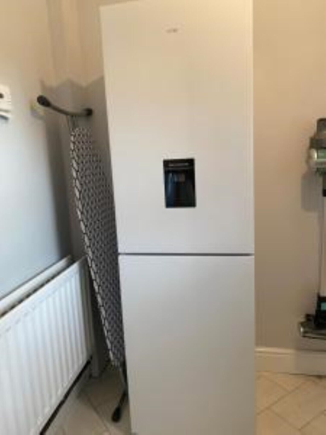 A white refrigerator with a water dispenser, a radiator, and a towel hanging on a rack.