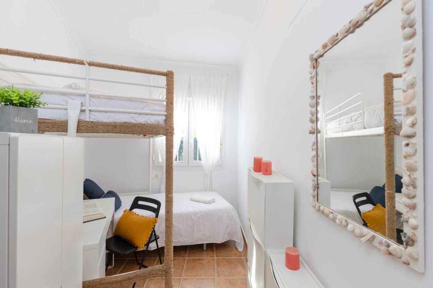 Una habitación con literas, un escritorio, una silla, un espejo y una planta pequeña.