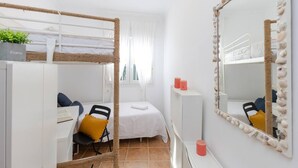 Ein Zimmer mit Etagenbetten, einem Schreibtisch, einem Stuhl, einem Spiegel und einer kleinen Pflanze.