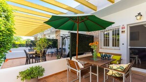 Eine Terrasse im Freien mit Tisch und Stühlen, einem grünen Sonnenschirm und Blumentöpfen.