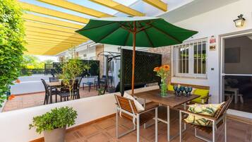Un patio exterior con una mesa, sillas, un paraguas verde y plantas en macetas.