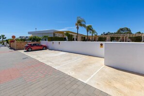 A parking area with a red car, white walls, and a clear blue sky.
